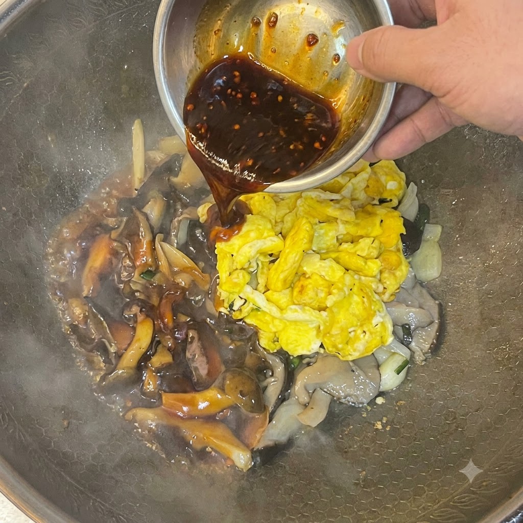 Une sauce foncée versée dun bol en métal sur les œufs brouillés et les champignons dans un wok.