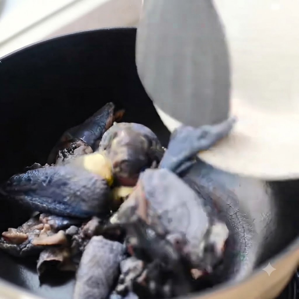 Morceaux de poulet à peau noire en train dêtre sautés dans une cocotte noire avec du gingembre.