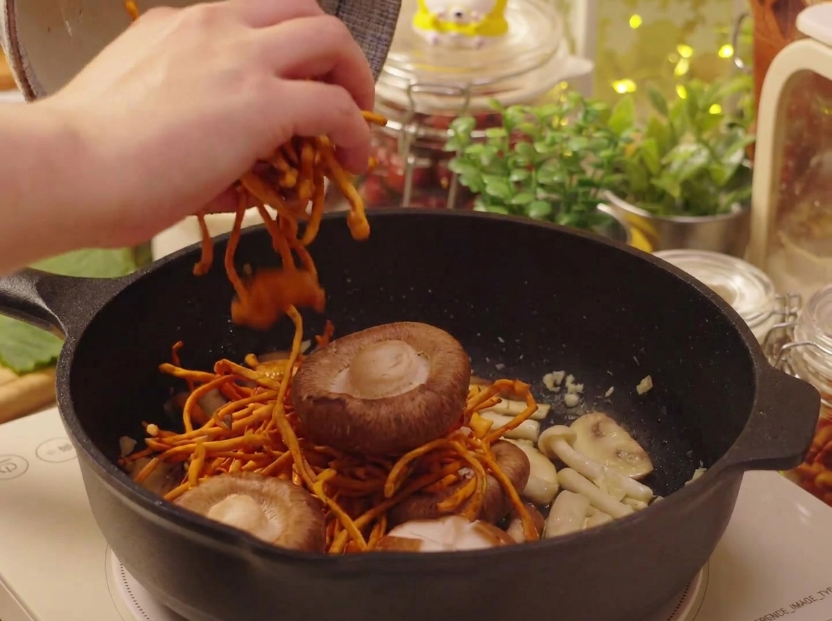 Des champignons shiitakes trempés et du cordyceps ajoutés dans la poêle.