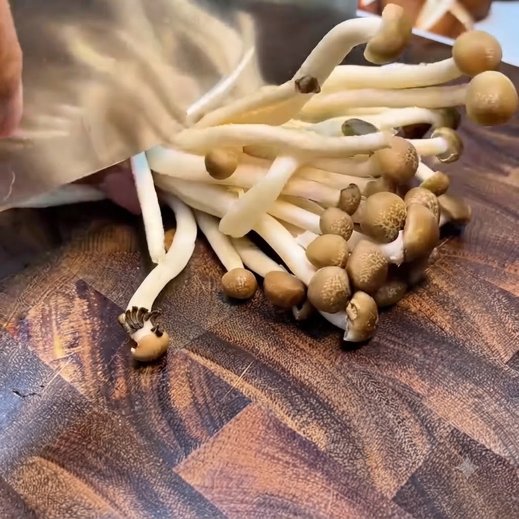Des champignons shimeji dont on coupe la grappe de racines avec un hachoir sur une planche en bois.