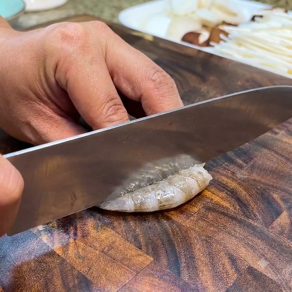 Des crevettes crues coupées et dénervées avec un couteau sur une planche à découper en bois.