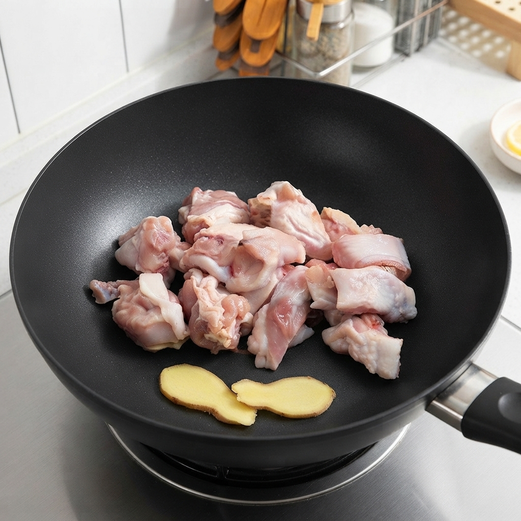 Morceaux de poulet cru et tranches de gingembre reposant dans un wok avant la cuisson.