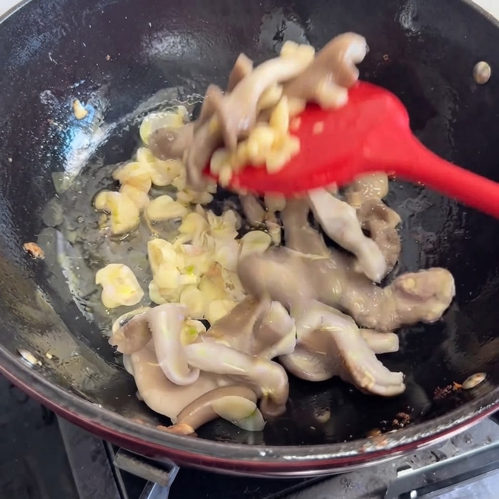 Des champignons frais ajoutés et remués dans la poêle avec les aromates à laide dune spatule rouge.