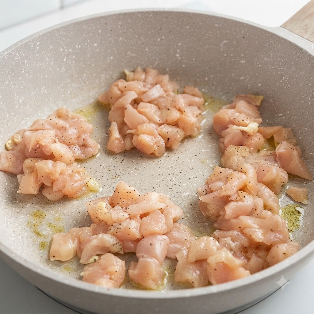 Morceaux de blancs de poulet marinés grésillant dans une poêle ronde à feu doux.