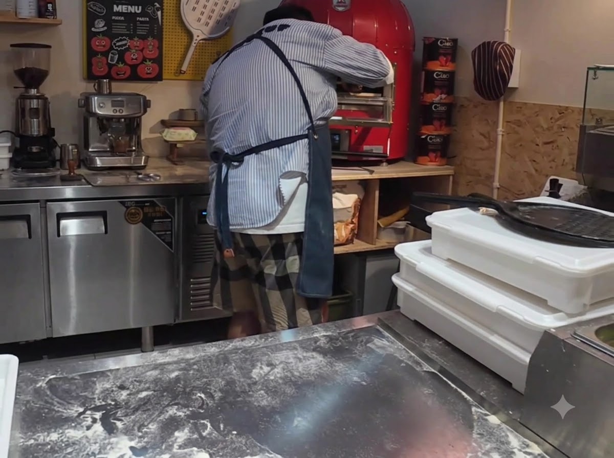 Une pizza en cours denfournement dans un four à pizza électrique commercial rouge vif à laide dune pelle à pizza.