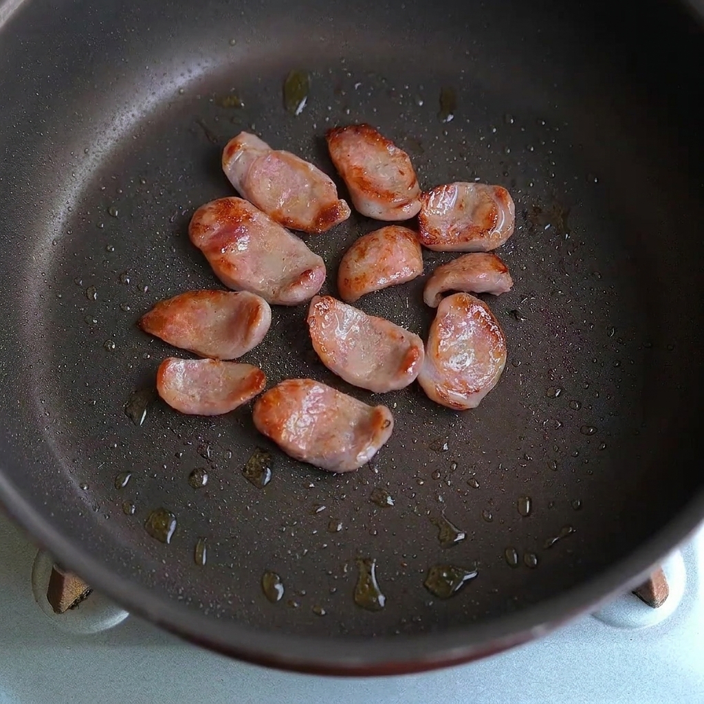 Des tranches de saucisse et des morceaux dail mélangés ensemble dans une poêle.