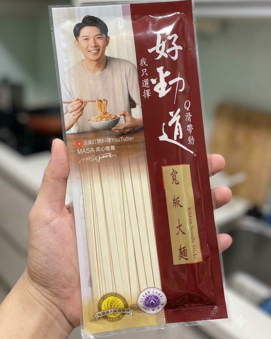 Un paquet de bâtonnets de nouilles larges Hao Jin Dao tenu devant un fond de cuisine.