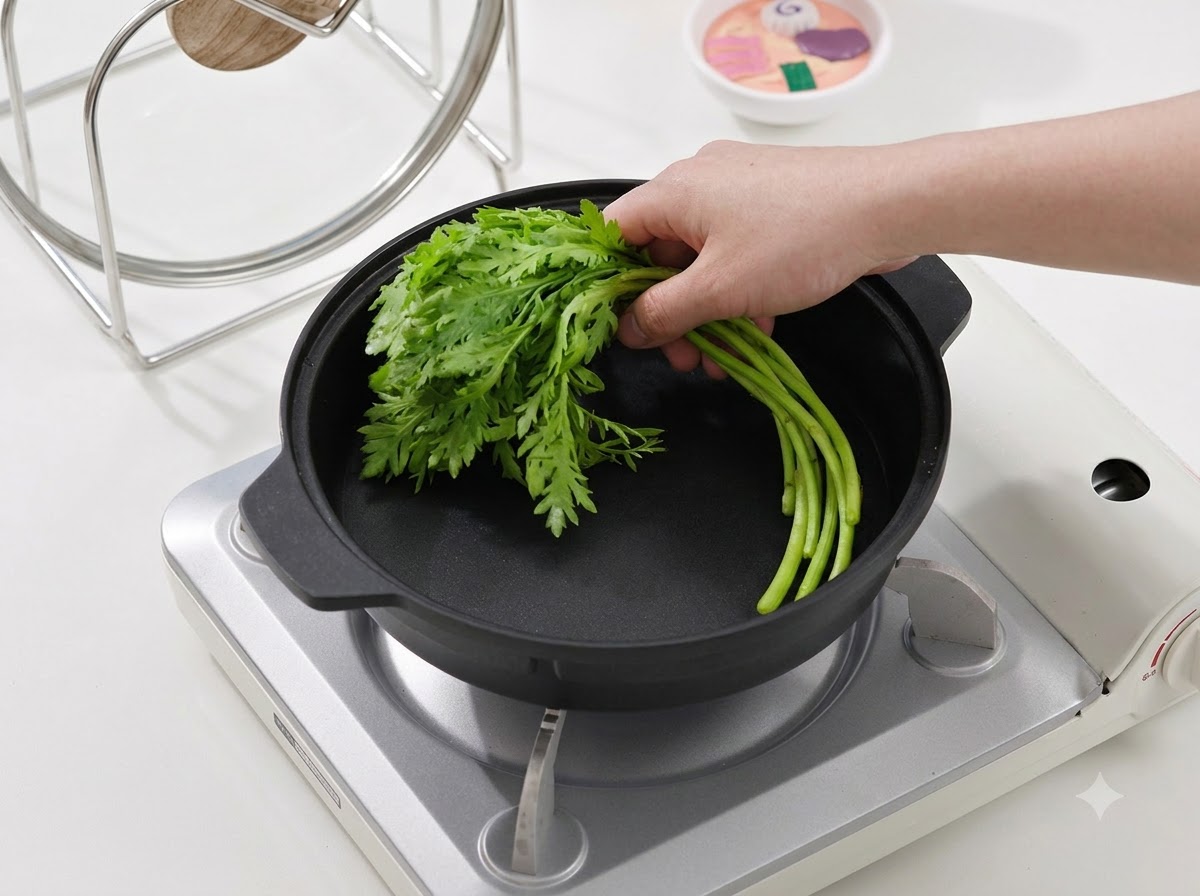 Une main plaçant un bouquet de légumes verts à feuilles fraîches dans une poêle de cuisson noire sur un poêle portable.