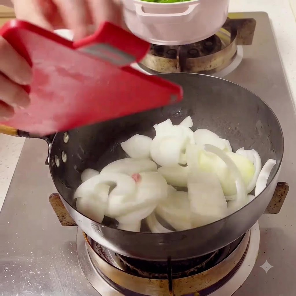 Des tranches doignon blanc versées dune planche à découper rouge dans un wok noir chaud sur une cuisinière.