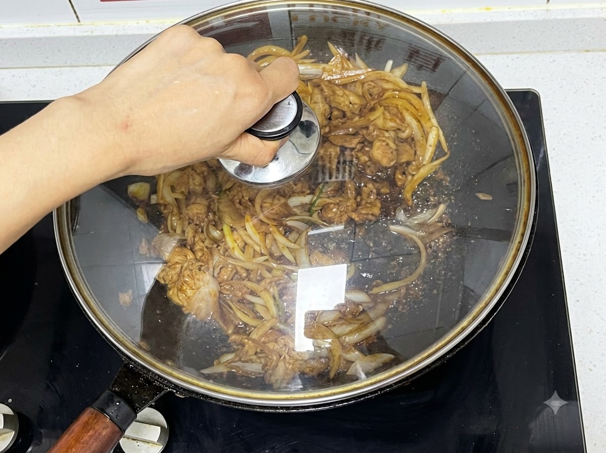 Un couvercle en verre posé sur un wok contenant du bœuf et des oignons en train de mijoter.