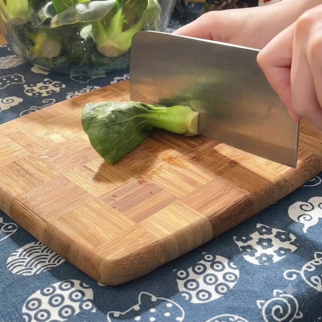 Jeunes pousses de légumes verts coupées en petits morceaux sur une planche à découper en bois à laide dun grand couteau de boucher.