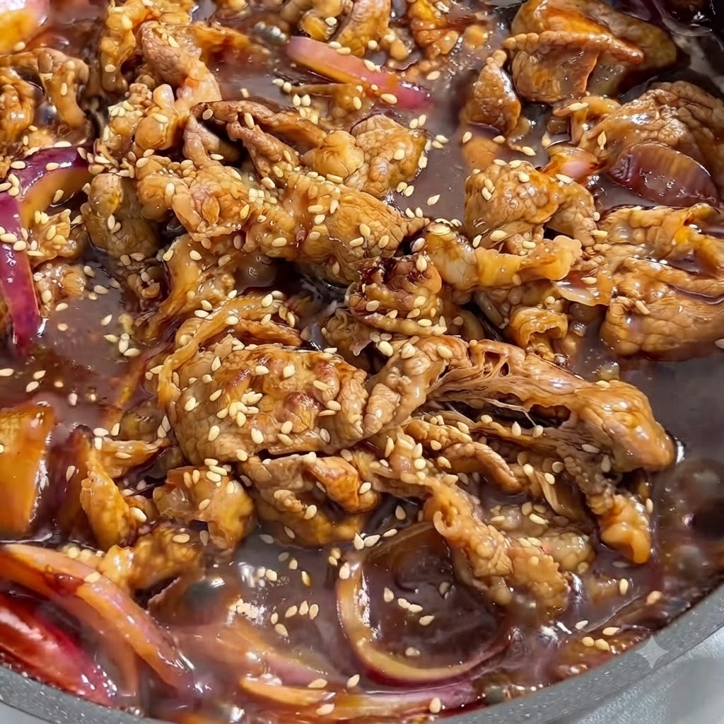 Gros plan sur du bœuf cuit et des oignons rouges mijotant dans une sauce sombre et savoureuse, parsemés de graines de sésame blanc.