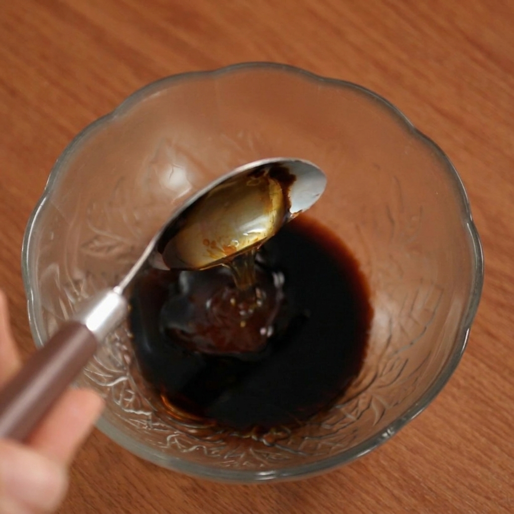 Du miel versé à la cuillère dans le mélange de sauce sombre à lintérieur dun bol en verre.