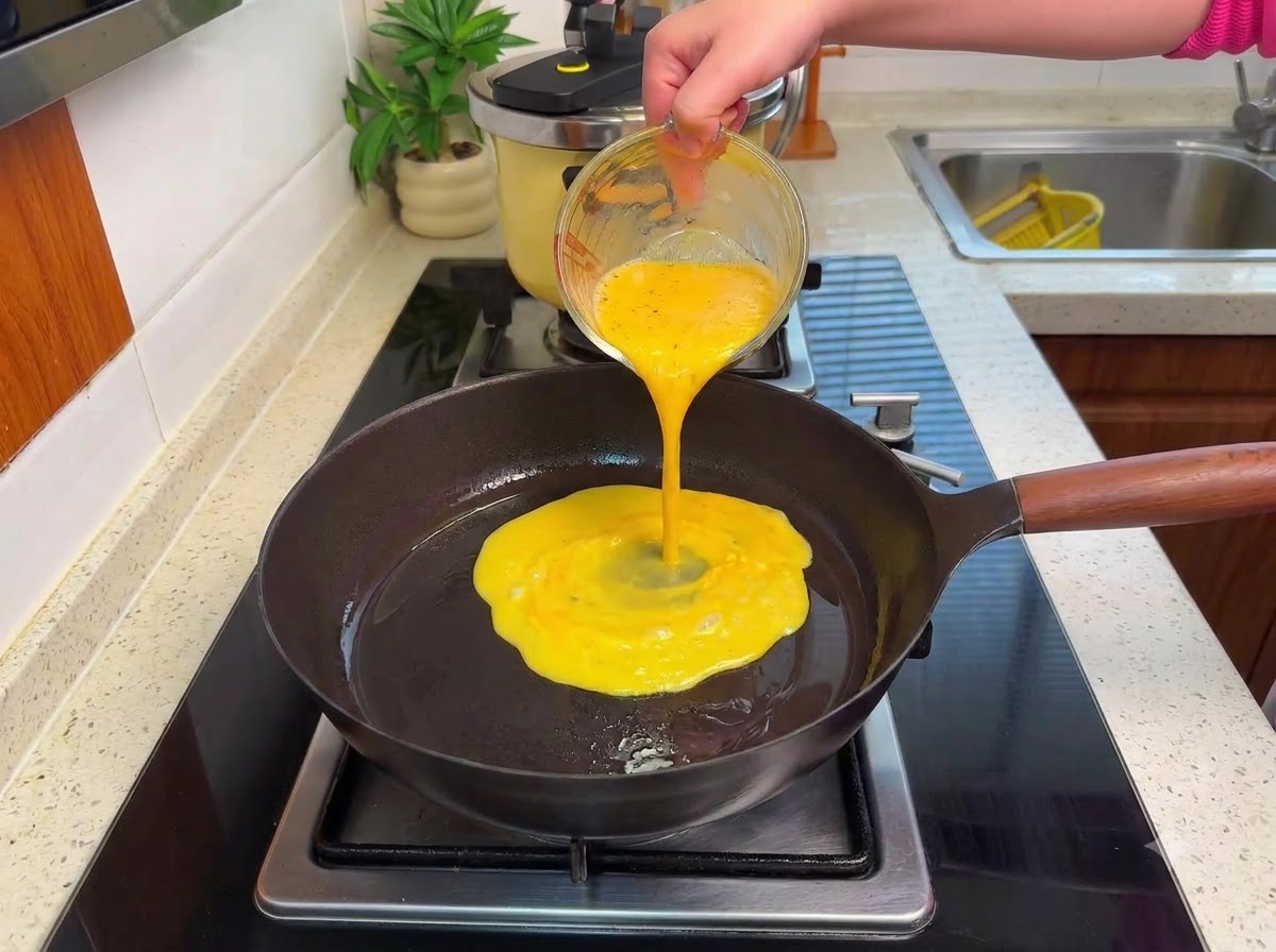 Des œufs battus versés dans une poêle chaude sur une cuisinière, formant des grumeaux moelleux à feu doux.