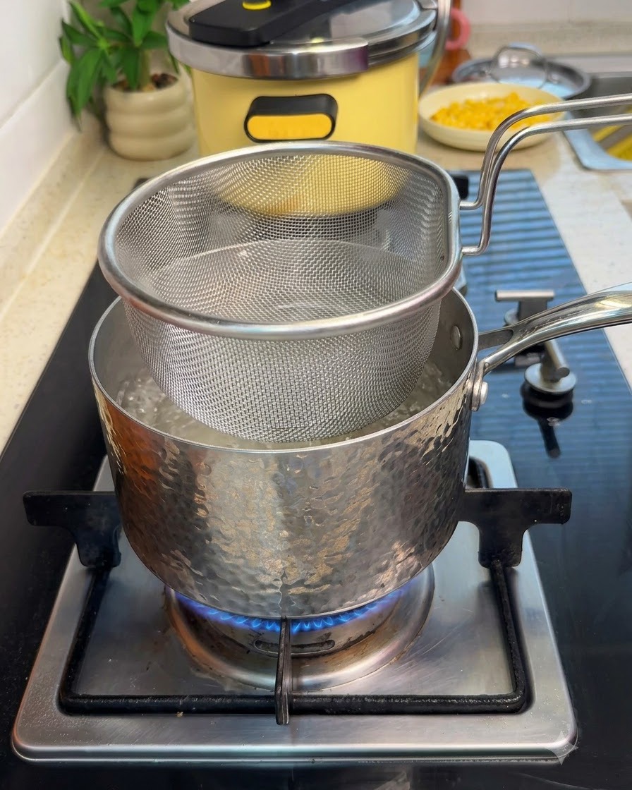 Un panier de passoire en mailles submergé dans une casserole deau bouillante sur une cuisinière avec des tranches de bœuf.