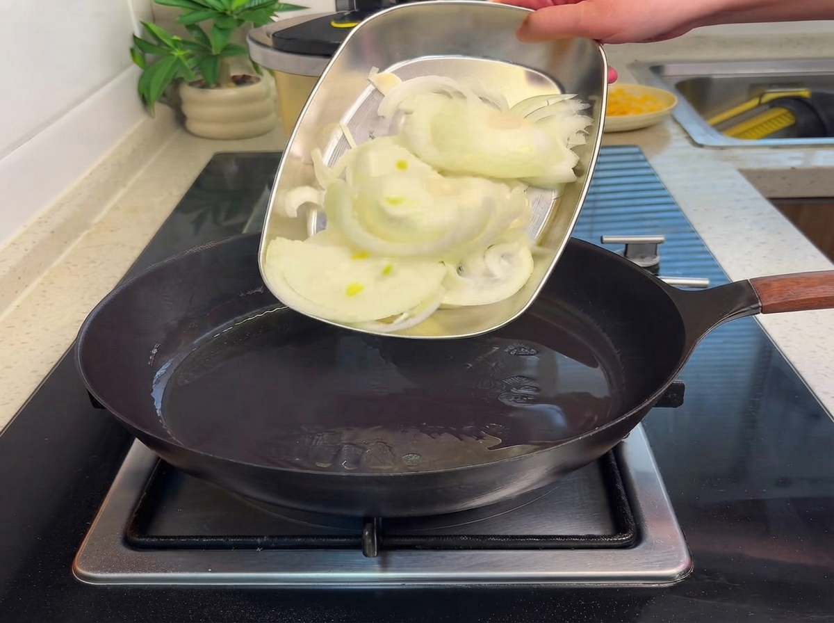 Des oignons tranchés glissés dun plateau en métal vers une poêle chaude contenant de lhuile.