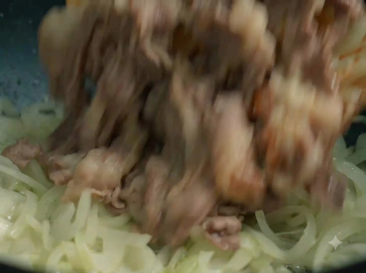 Des tranches de bœuf cuites remises dans le wok avec les oignons sautés.