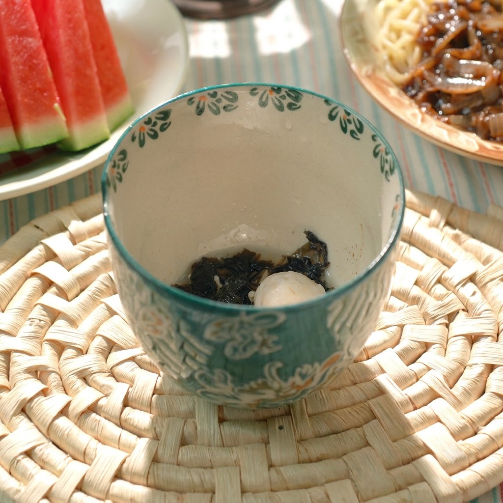 Une boulette de porc cuite et des algues dans un bol à soupe en céramique à motifs.