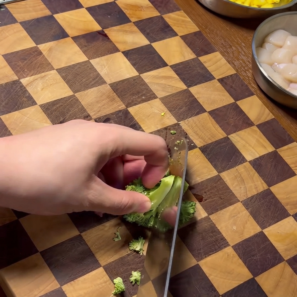 Une main utilisant un couteau pour hacher des bouquets de brocoli sur une planche à découper en bois à motifs damés.
