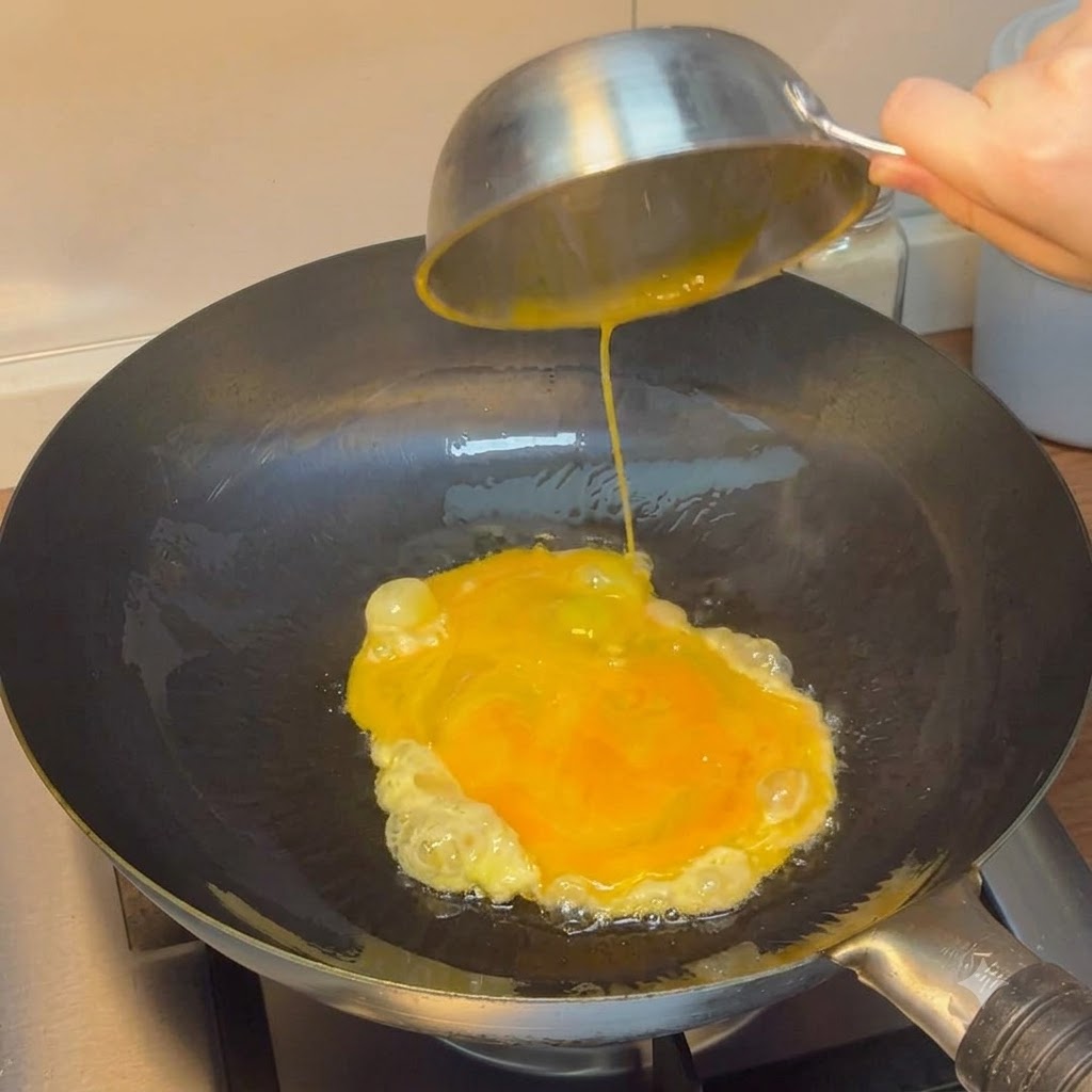 Œufs battus versés dun bol en acier dans un wok chauffé.