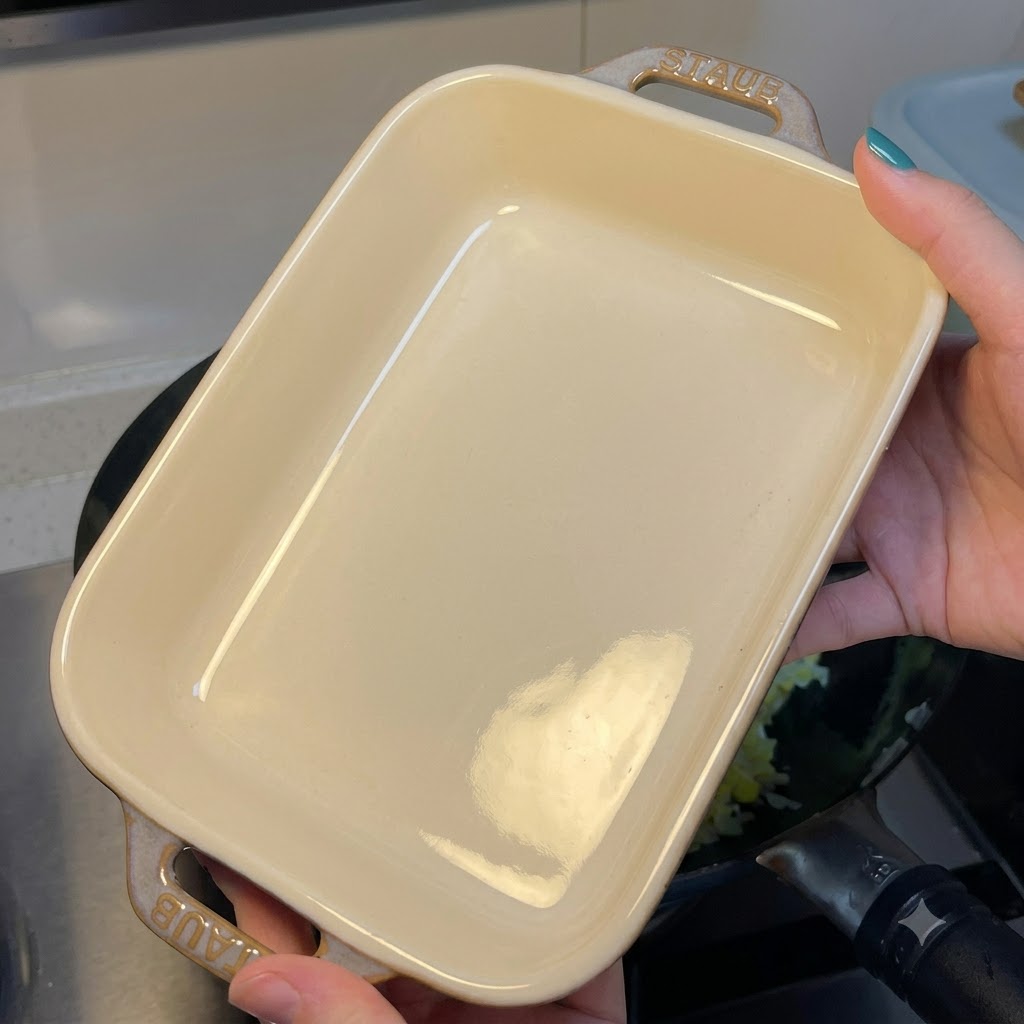 Une personne tenant un plat à gratin rectangulaire en céramique blanche vide au-dessus dun wok contenant du riz sauté aux œufs.