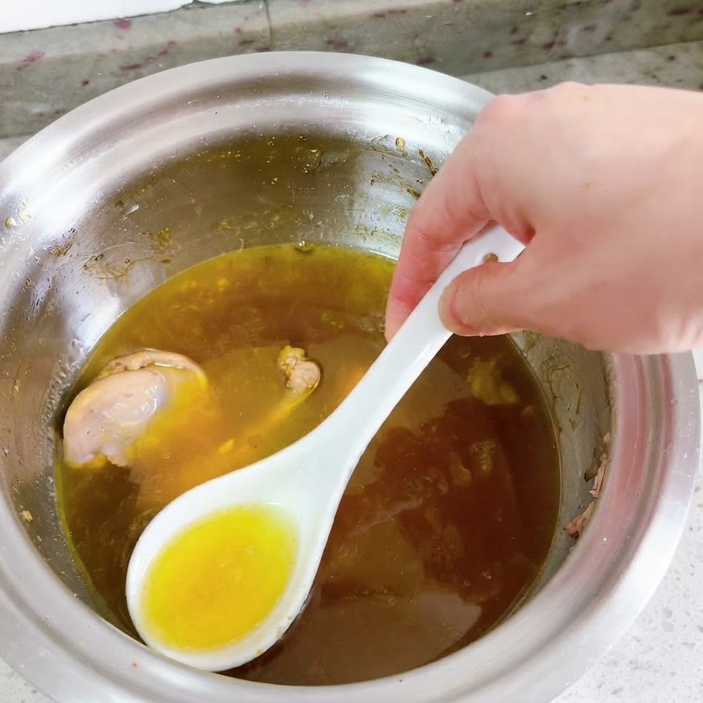 Une cuillère blanche retirant lhuile jaune vif de la surface dune soupe de canard frémissante.