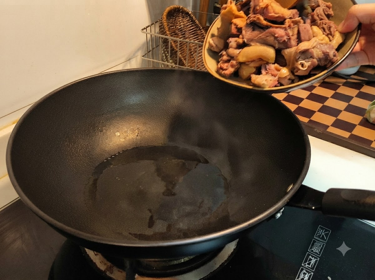 Une main versant des morceaux de canard blanchis dune assiette dans un wok noir chaud avec de lhuile.