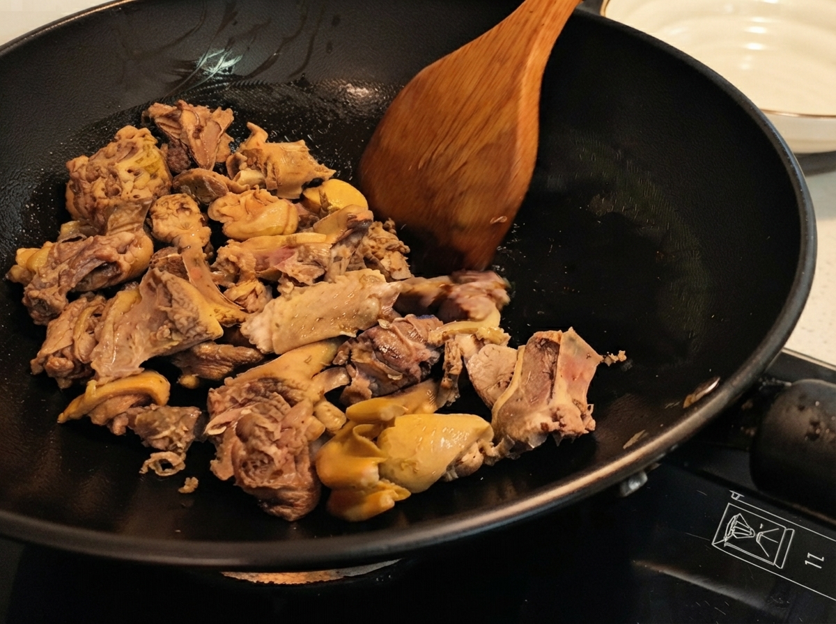 Morceaux de canard remués dans un wok avec une spatule en bois, montrant une peau dorée.