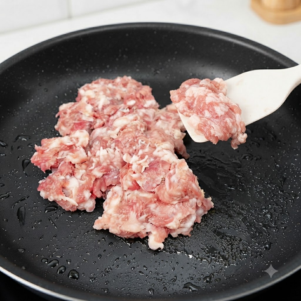 Porc haché cru en train dêtre ajouté et sauté dans une poêle noire avec une spatule en silicone.