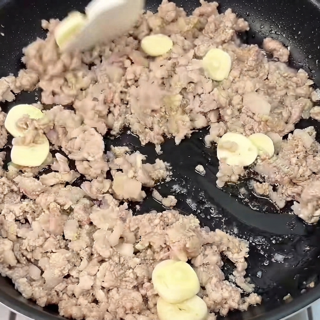 Gingembre et ail tranchés mélangés et sautés avec du porc haché doré dans une poêle.