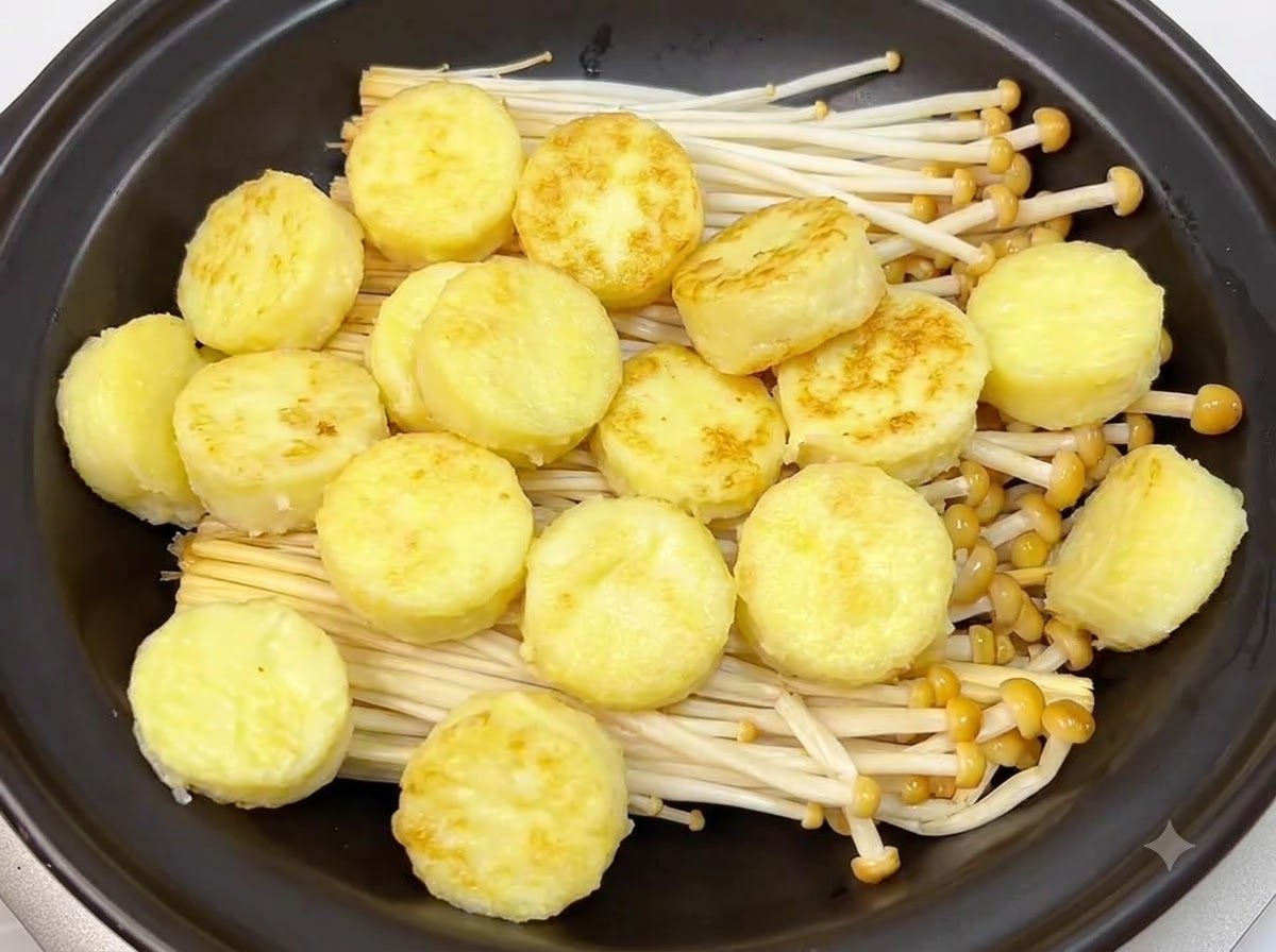 Rondelles de tofu japonais dorées et poêlées disposées soigneusement sur les champignons enoki à lintérieur dun plat en terre cuite noir.