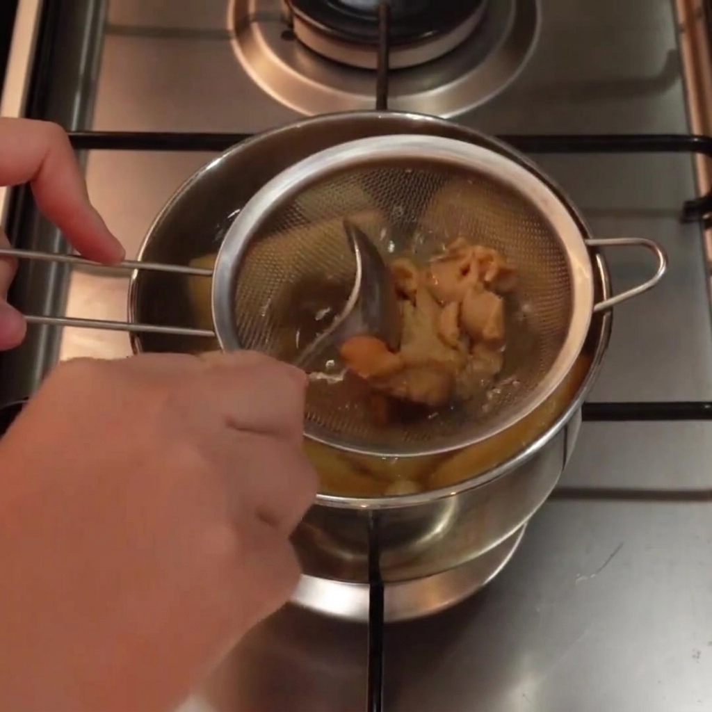 De la pâte de miso blanc mélangée dans une petite passoire immergée dans le bouillon chaud à laide dune cuillère.
