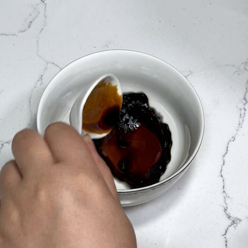 Ingrédients de la sauce comprenant sauce soja, sauce huître, sucre et fécule mélangés avec de leau dans un bol blanc à laide dune cuillère.