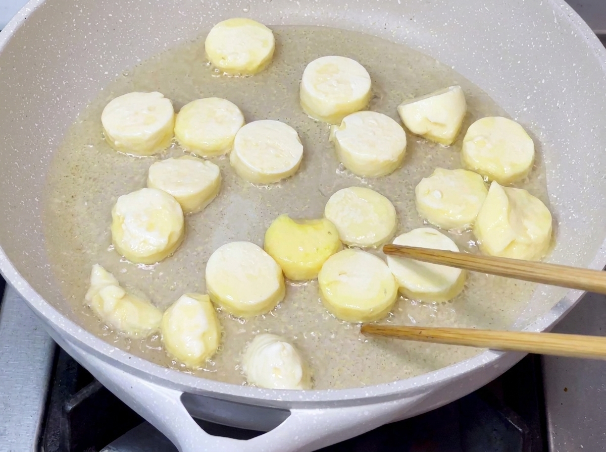 Morceaux de tofu en train de frire dans de lhuile de cuisson chaude dans une poêle jusquà ce que leur surface devienne dorée et croustillante.