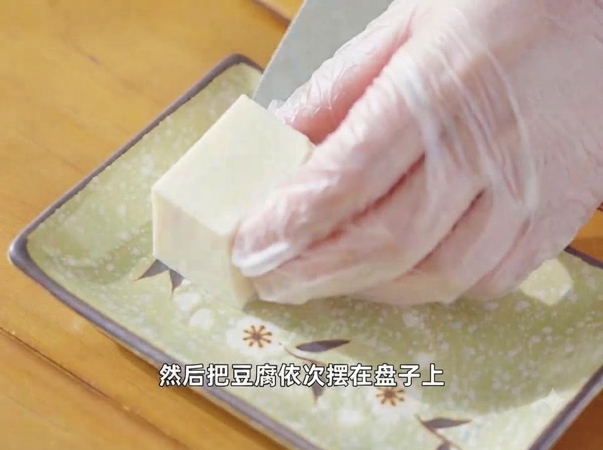 Des mains gantées disposant un morceau de tofu soyeux coupé sur une assiette verte décorative.