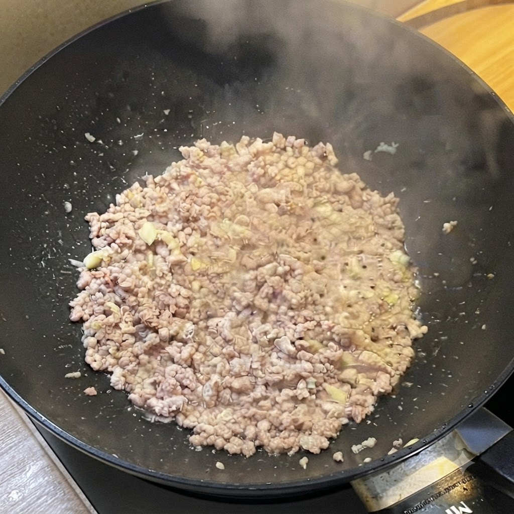 Un wok rempli de viande hachée dorée dégageant de la vapeur, assaisonnée avec des sauces liquides.