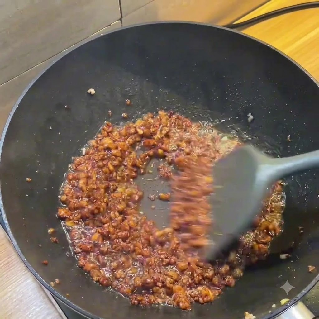 Un wok sombre montrant une riche sauce brune au porc haché remuée avec une spatule grise.