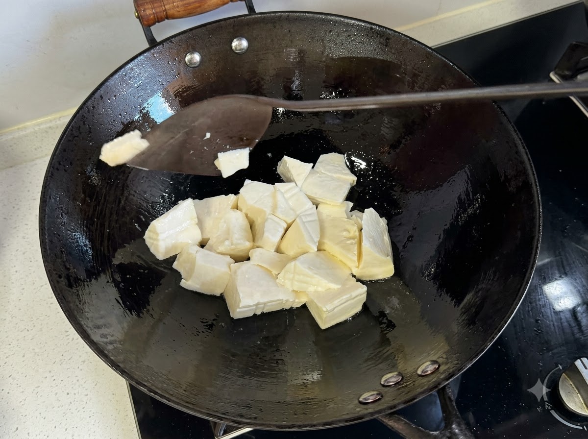 Une spatule coupant des morceaux de tofu moelleux directement à lintérieur dun wok de friture chaud.