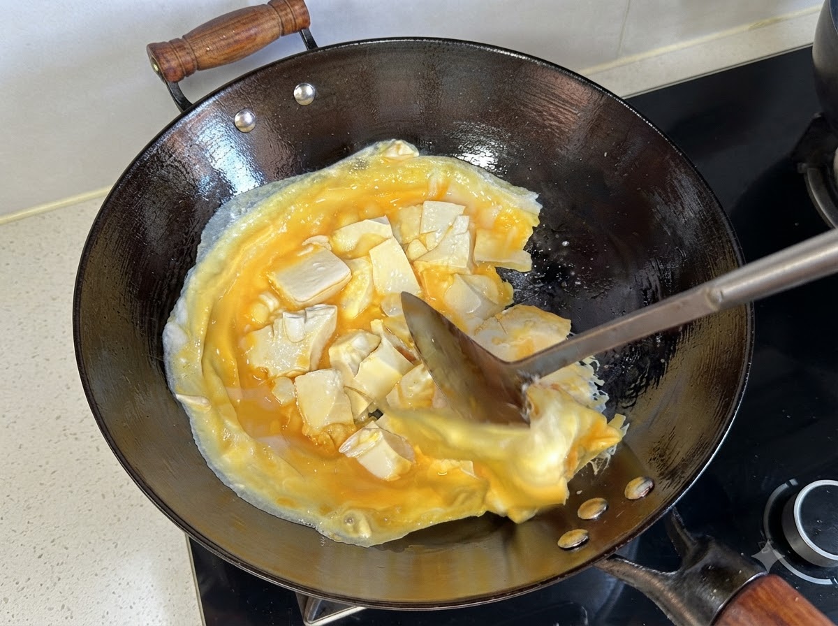 Une spatule soulevant et retournant la couche cuite dœufs et de tofu dans le wok.