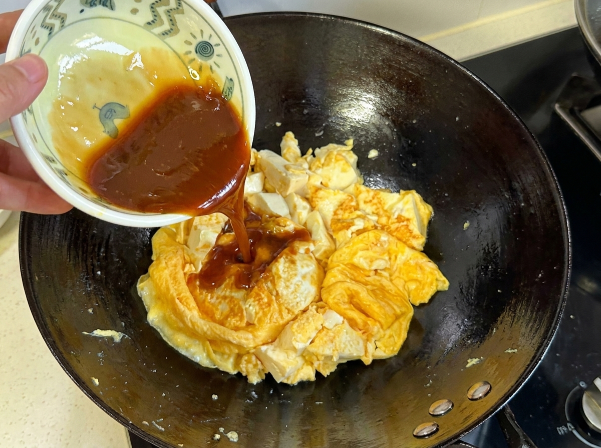 De la sauce marron foncé versée dun petit bol sur le mélange dœufs et de tofu cuit dans le wok.