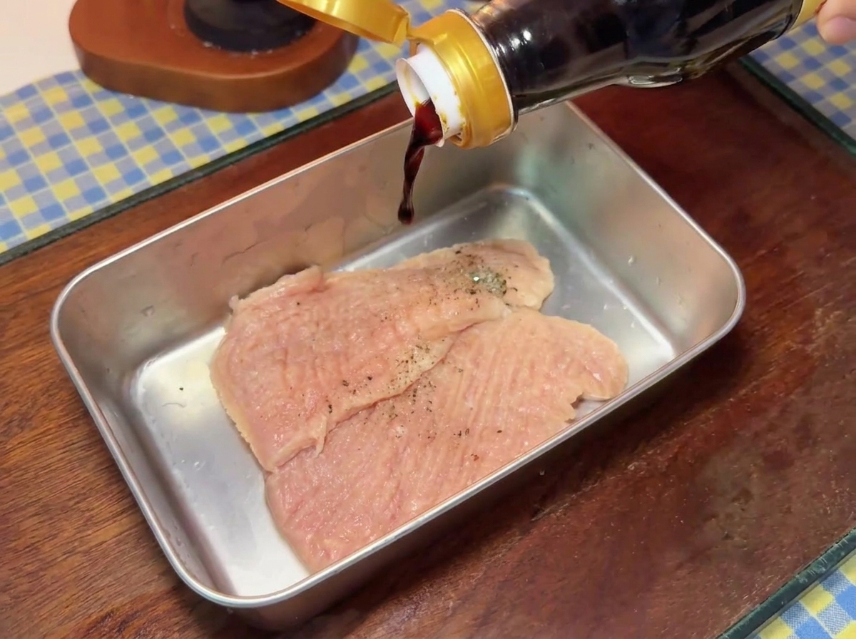 De la sauce soja foncée versée dune bouteille en verre sur des côtelettes de porc assaisonnées dans un plateau en métal.
