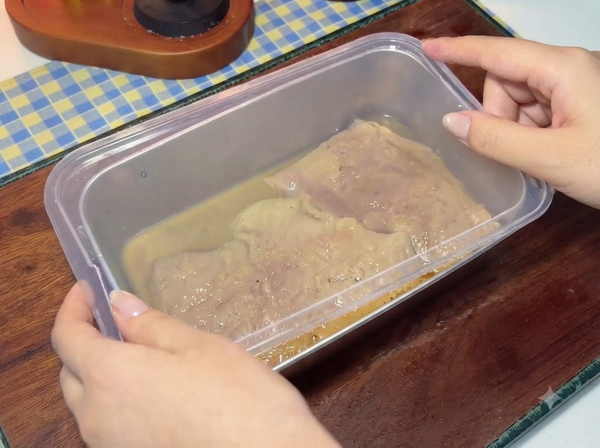 Un couvercle en plastique en train dêtre placé sur un récipient rempli de côtelettes de porc marinées et de liquide.