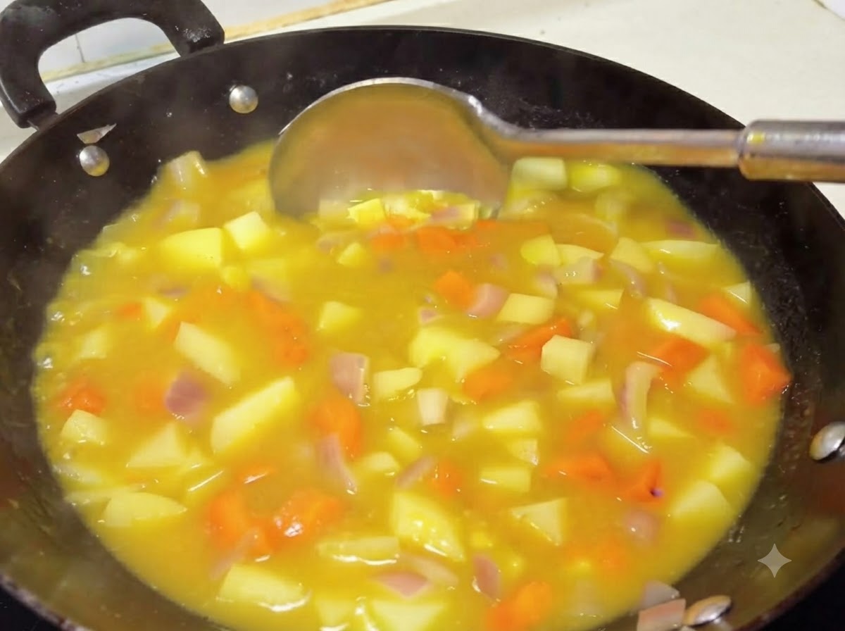 Une louche remuant une sauce curry jaune épaisse et riche avec des pommes de terre et des carottes dans un wok.