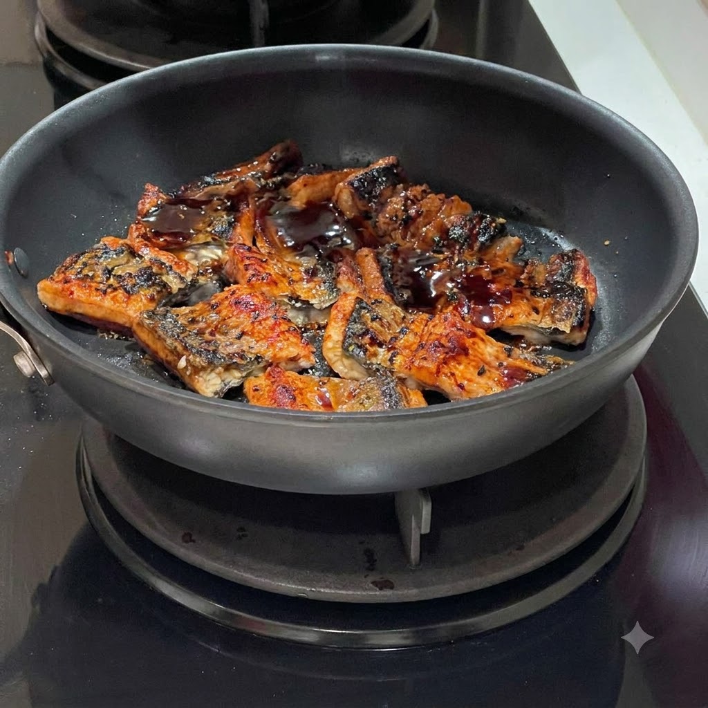De la sauce sombre versée en filet sur des morceaux danguille grésillants dans une poêle.