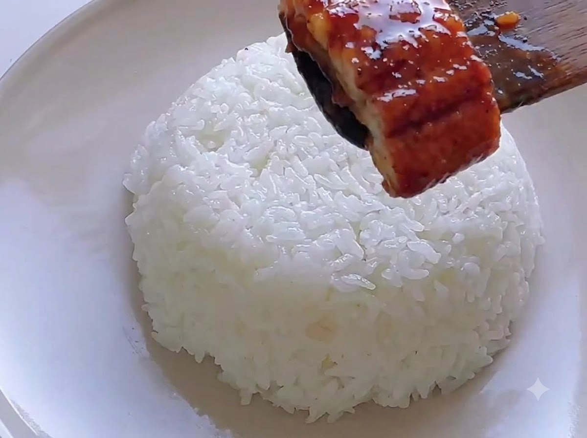 Une spatule en bois plaçant un morceau danguille glacé sur un dôme de riz blanc.
