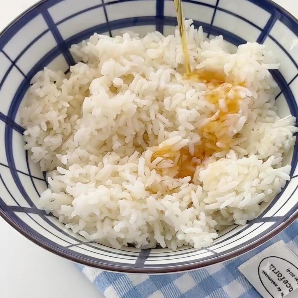 De lhuile de sésame versée en filet dans un grand bol rempli de riz blanc cuit.