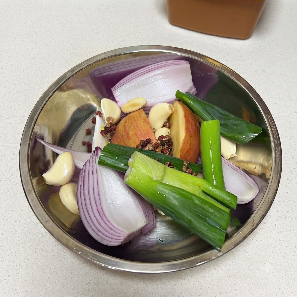 Oignons verts frais coupés dans un bol en métal rempli doignon rouge, de pomme, de gousses dail, de grains de poivre et dune feuille de laurier.