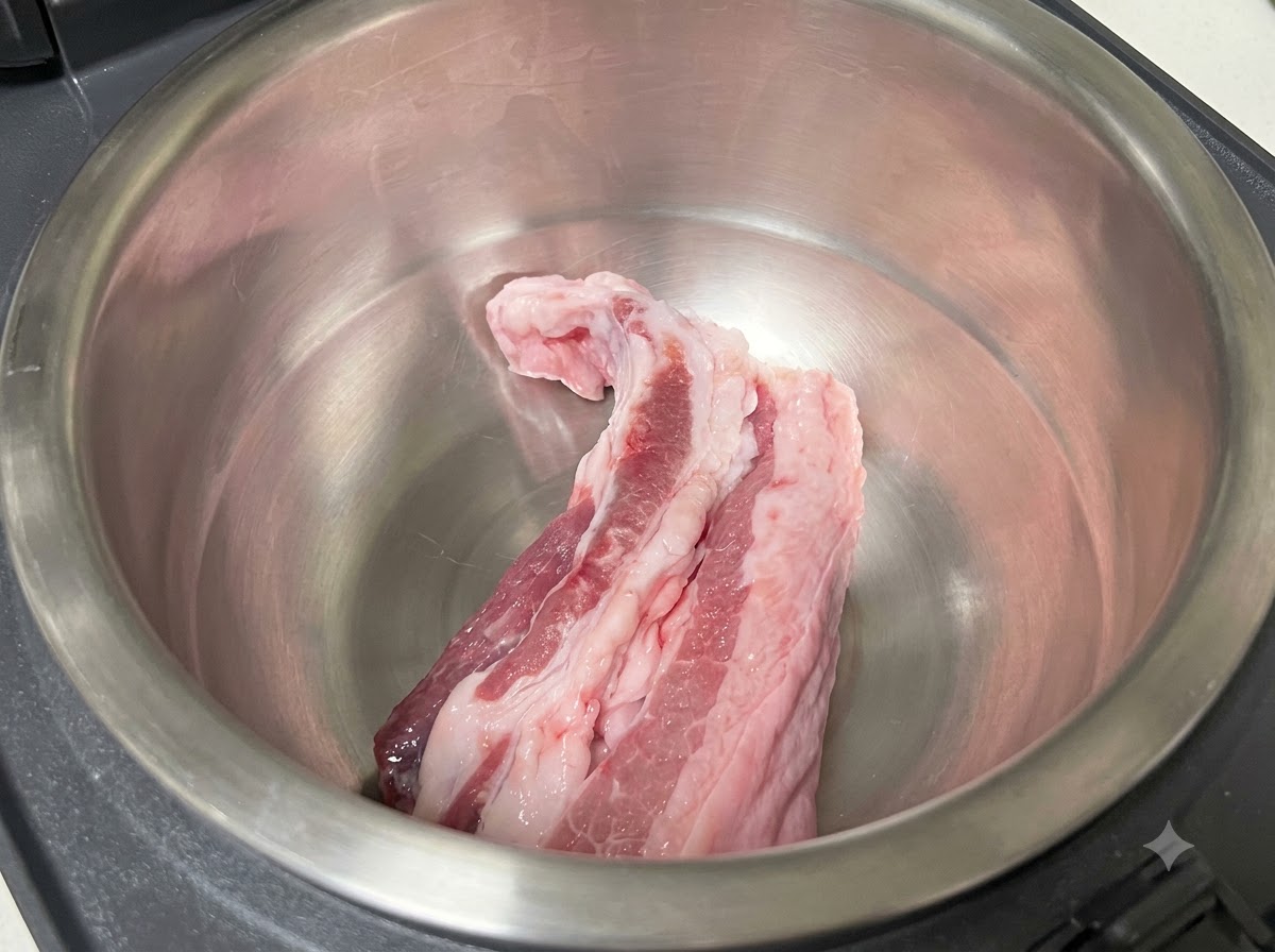 Tranches de poitrine de porc crues reposant à lintérieur du pot intérieur en acier inoxydable dun cuiseur à riz.