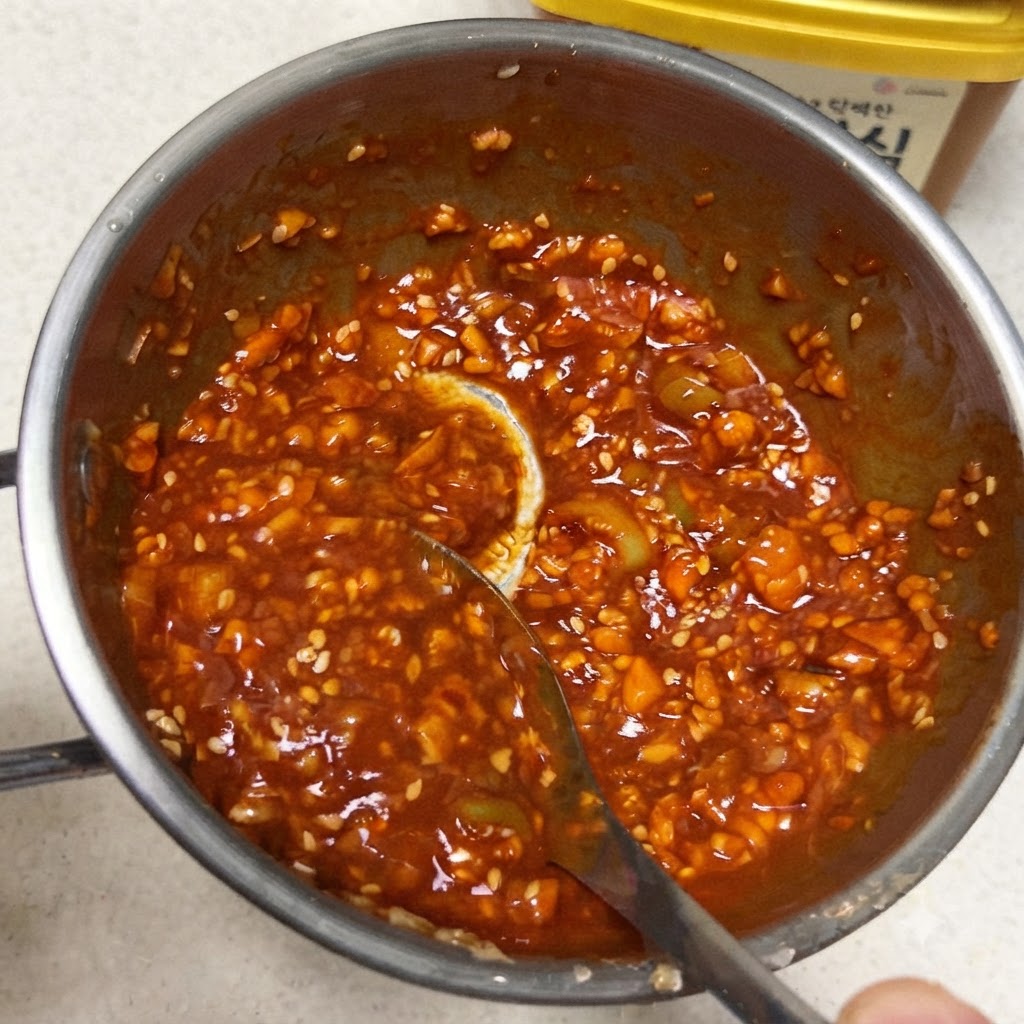 Une cuillère mélangeant une sauce trempette coréenne rouge vif et épaisse à lintérieur dune petite poêle en métal.