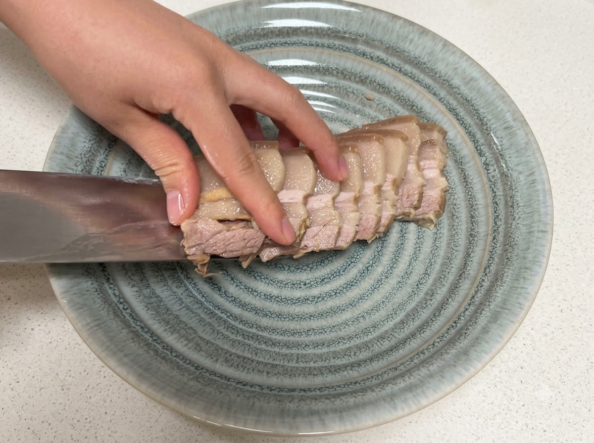 Tranches de poitrine de porc cuite transférées sur une assiette grise texturée avec un couteau.